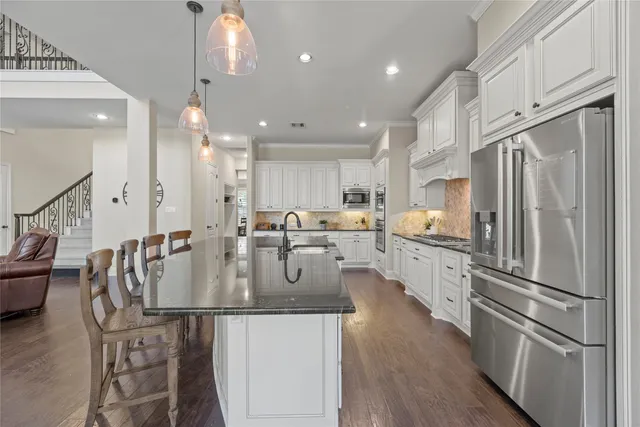 a kitchen with stainless steel appliances granite countertop a refrigerator a oven a sink a dining table and chairs with wooden floor