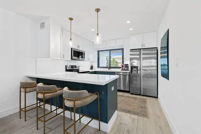 a kitchen with stainless steel appliances granite countertop a sink a stove a refrigerator and island with wooden floor