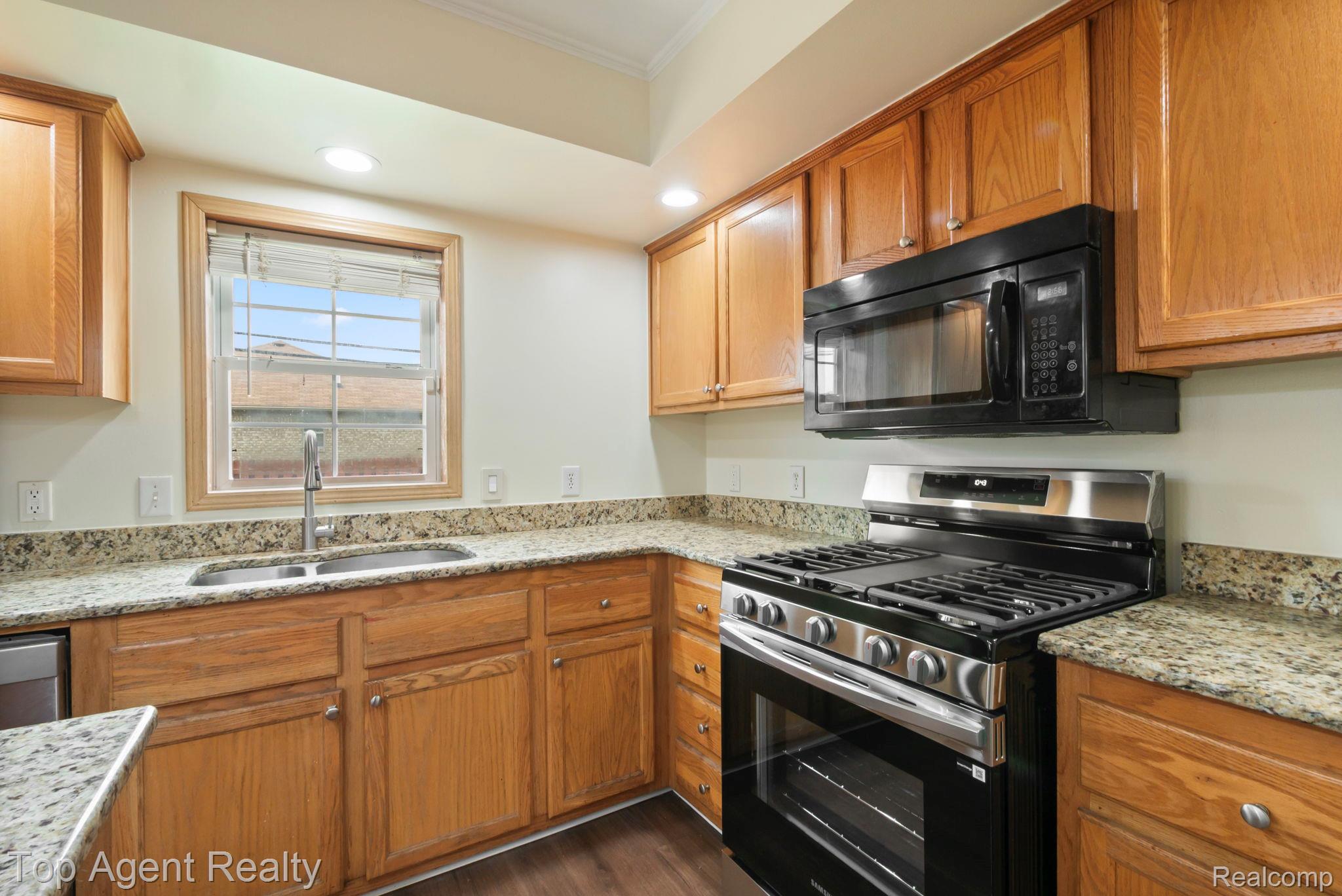 2018 John R Road Troy, MI 48083 - Photo 6 of 30 Kitchen featuring stainless steel gas range, light stone counters, black microwave, crown molding, and wood finish cabinets