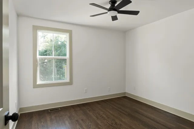 an empty room with wooden floor fan and windows