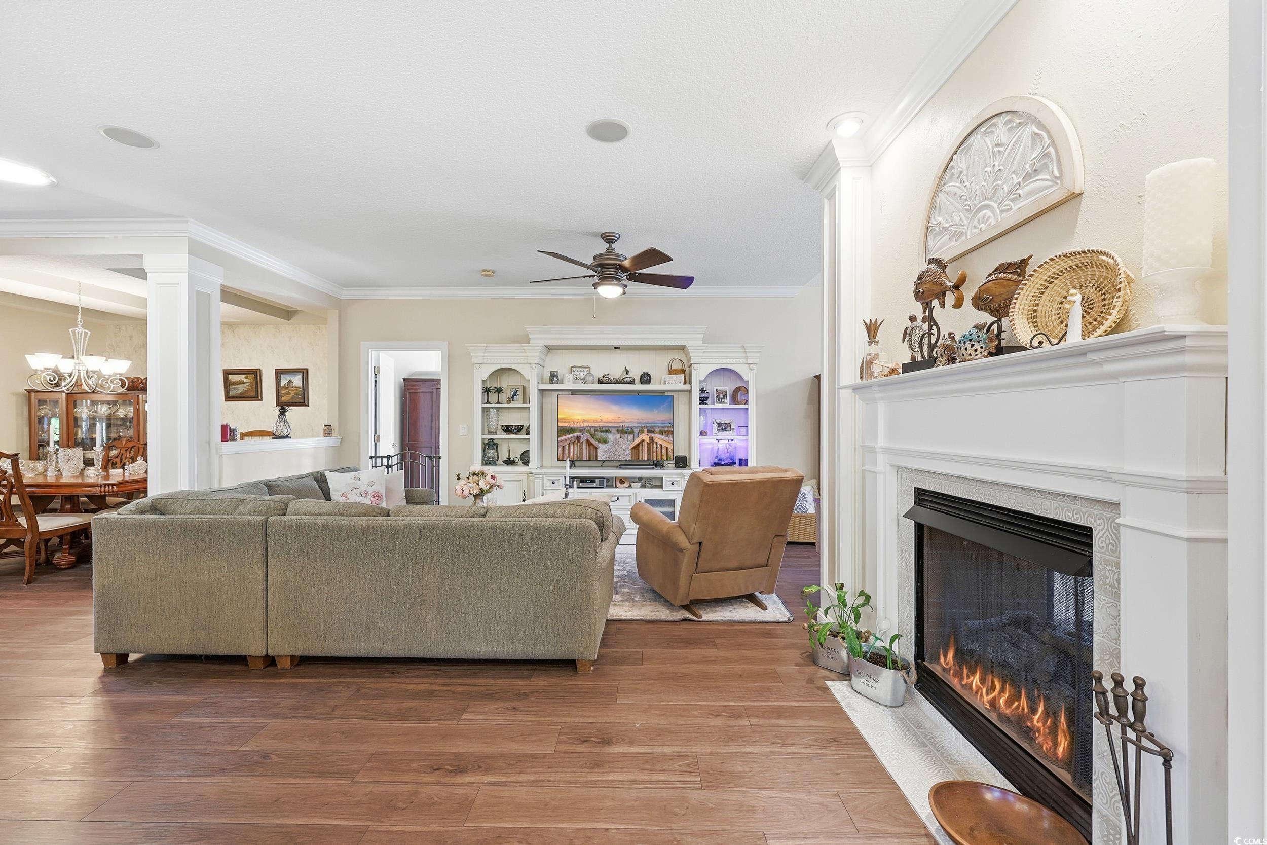 452 Deer Watch Circle Longs, SC 29568 - Photo 17 of 39 Living area with a fireplace with flush hearth, wood finished floors, crown molding, a ceiling fan, and a chandelier
