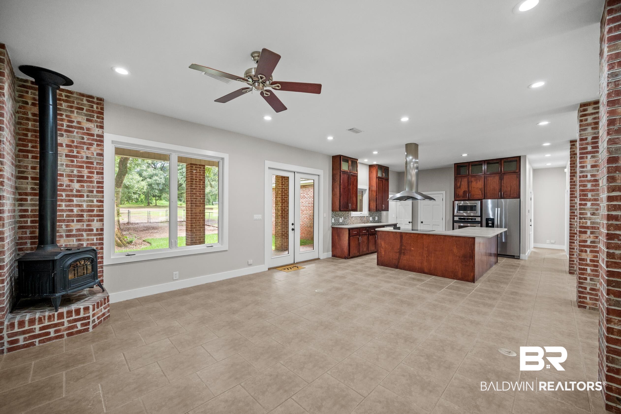 15031 Timber Ridge Drive Loxley, AL 36551 - Photo 13 of 43 Kitchen featuring a wood stove, stainless steel refrigerator with ice dispenser, an island with sink, island exhaust hood, and light tile patterned floors