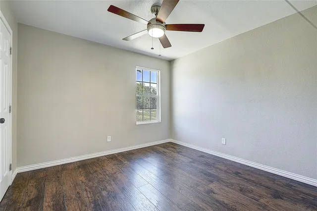 an empty room with wooden floor chandelier fan and windows