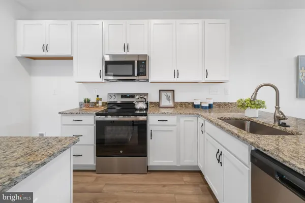 a kitchen with granite countertop a sink stainless steel appliances and white cabinets