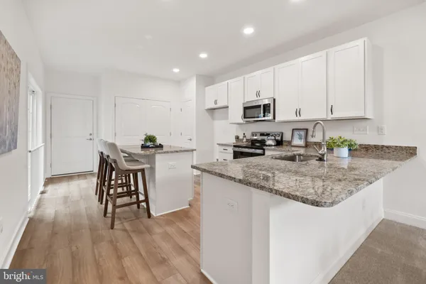 a kitchen with stainless steel appliances granite countertop a stove a sink a microwave a refrigerator and white cabinets with wooden floor