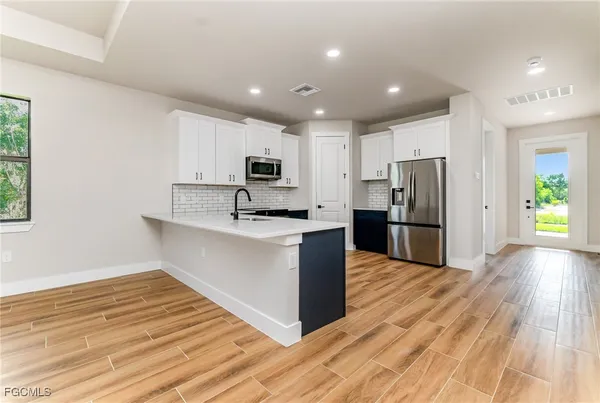 a large kitchen with kitchen island a sink dishwasher a refrigerator and a stove with wooden floor