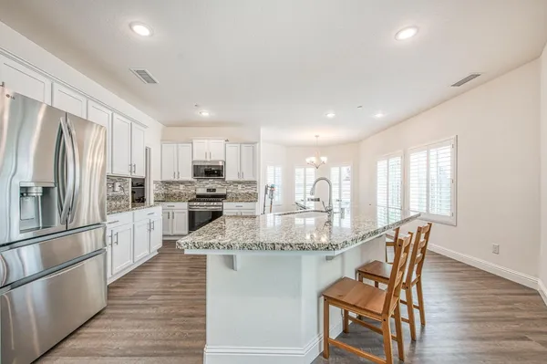a kitchen with stainless steel appliances granite countertop a dining table chairs refrigerator and sink