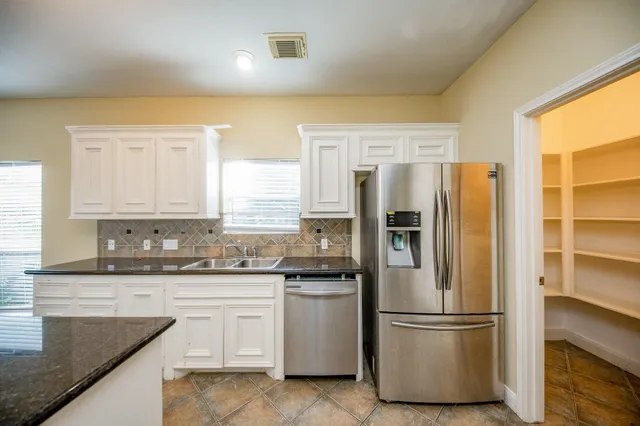 a kitchen with stainless steel appliances granite countertop a refrigerator a sink and white cabinets