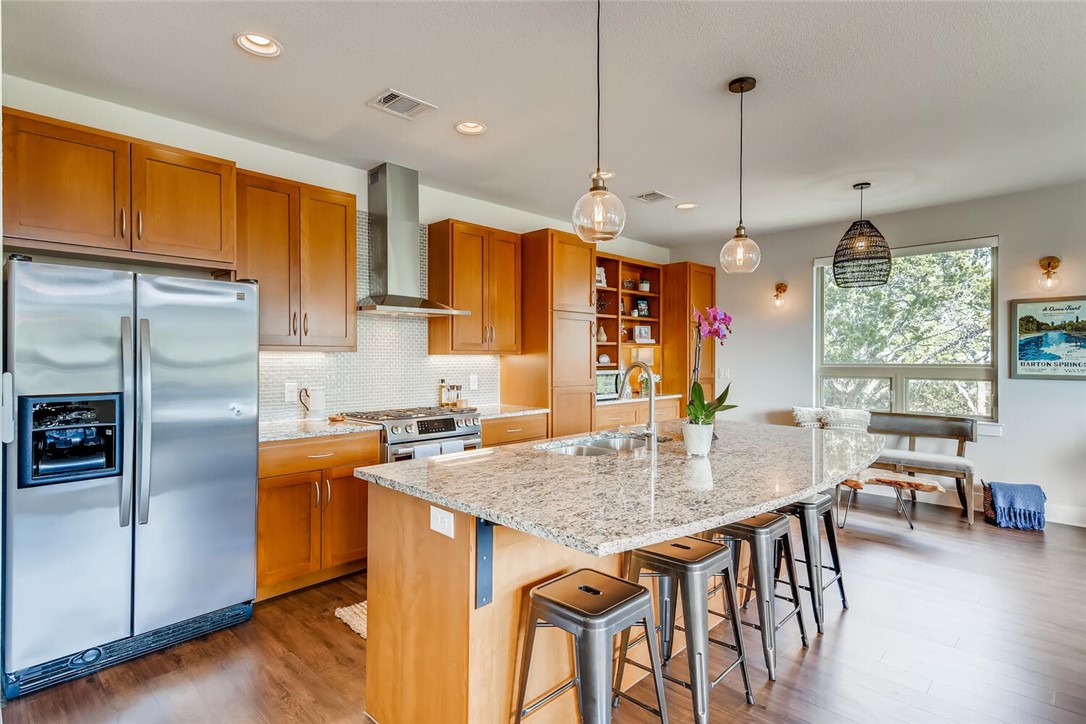 a kitchen with stainless steel appliances granite countertop a kitchen island a stove a refrigerator a dining table and chairs with wooden floor