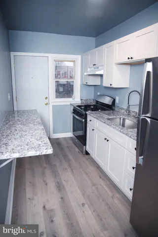 a kitchen with stainless steel appliances granite countertop a stove a sink and white cabinets with wooden floor