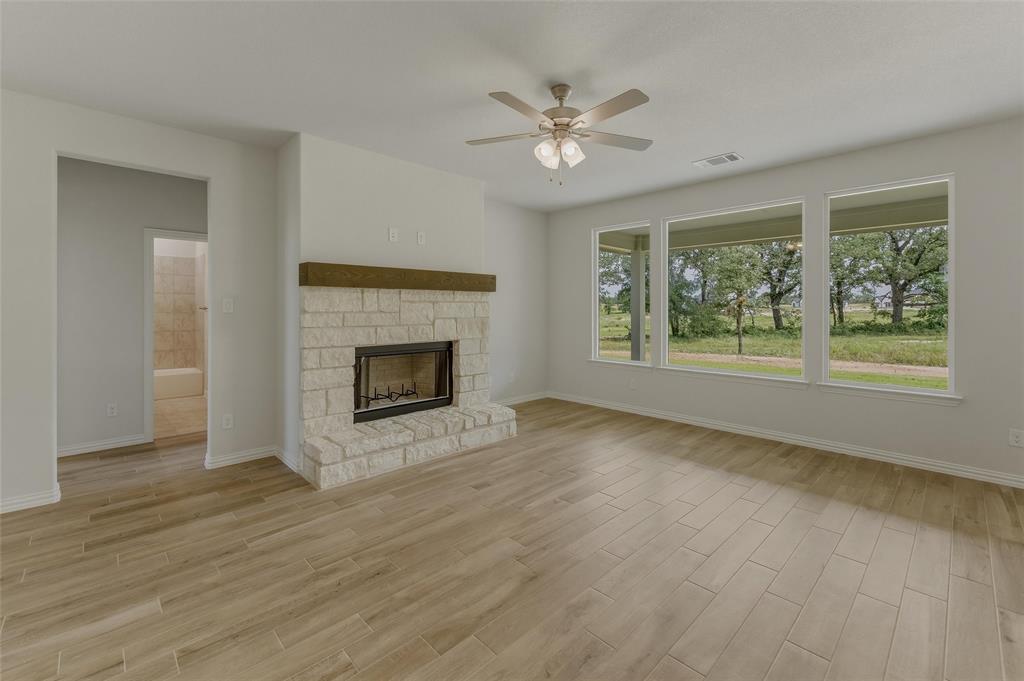 156 Oak Grv Way Springtown, TX 76082 - Photo 8 of 25 Spacious living area featuring wood-finish flooring, a stone fireplace with a wood mantel, and a ceiling fan