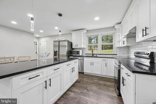 a kitchen with granite countertop white cabinets white appliances a sink and a window