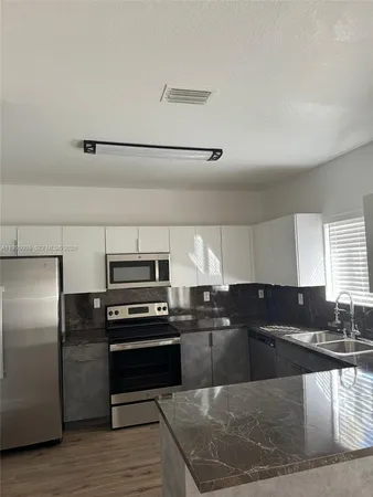 a kitchen with granite countertop a refrigerator and a stove top oven
