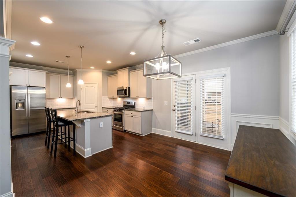 6622 Trailblazer Road Flowery Branch, GA 30542 - Photo 9 of 51 a kitchen with stainless steel appliances kitchen island granite countertop a stove a sink dishwasher a refrigerator and white cabinets with wooden floor