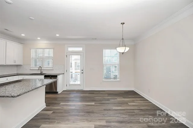 a large kitchen with granite countertop a stove top oven a sink dishwasher and white cabinets with wooden floor