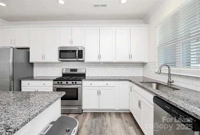 a kitchen with granite countertop a sink a stove top oven and cabinetry