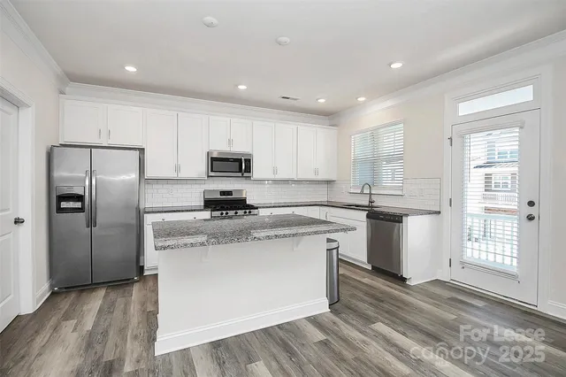 a kitchen with stainless steel appliances granite countertop a refrigerator a sink dishwasher a stove and white countertops with wooden floor