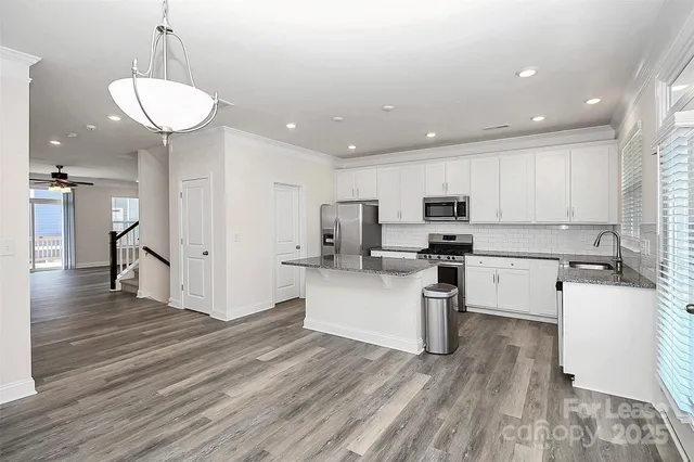 a kitchen with stainless steel appliances granite countertop a refrigerator a stove oven a sink dishwasher and white cabinets with wooden floor