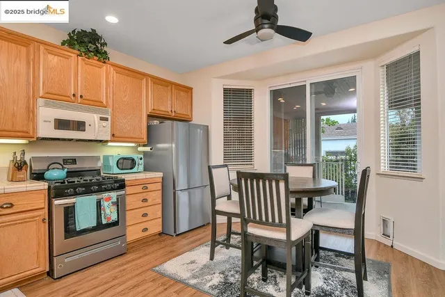 a kitchen with stainless steel appliances granite countertop a stove a refrigerator a kitchen island a dining table and chairs with wooden floor