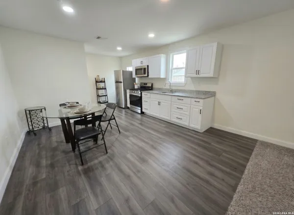 a kitchen with stainless steel appliances kitchen island granite countertop a stove a sink a refrigerator and white cabinets with wooden floor