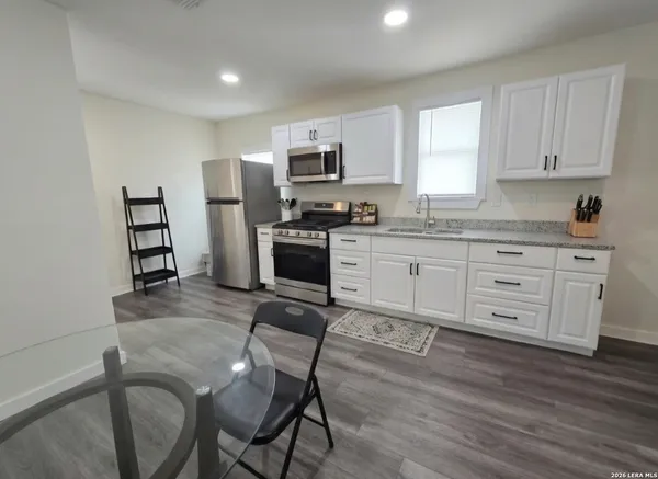 a kitchen with stainless steel appliances granite countertop a stove top oven a sink dishwasher a dining table and chairs with wooden floor