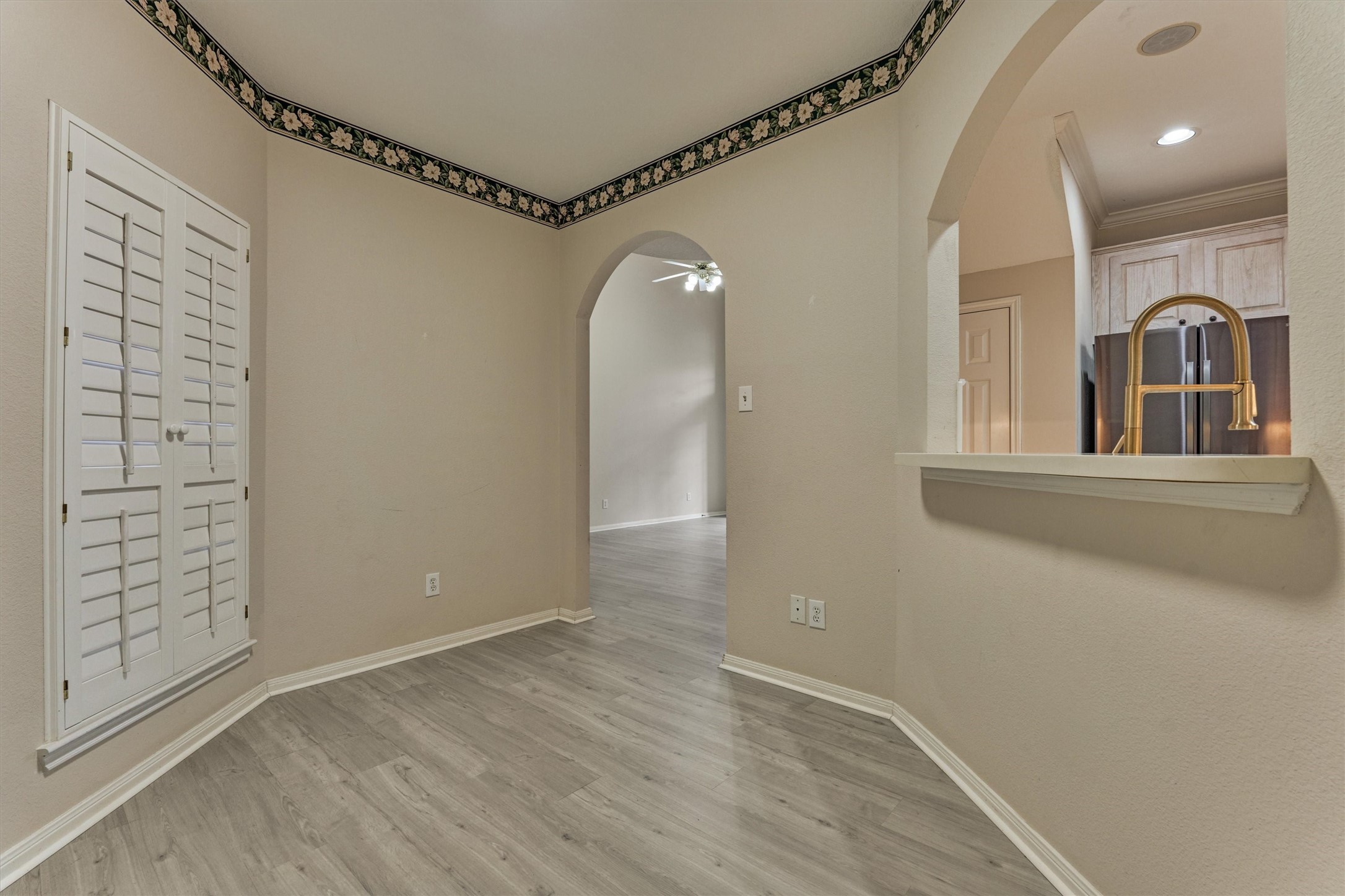 14420 Walters Road, Unit 26 Houston, TX 77014 - Photo 12 of 45 This room features light wood-look flooring, neutral walls, and a decorative border. It includes a window with white shutters and a passthrough to the kitchen. Perfect for a small dining area or office space.