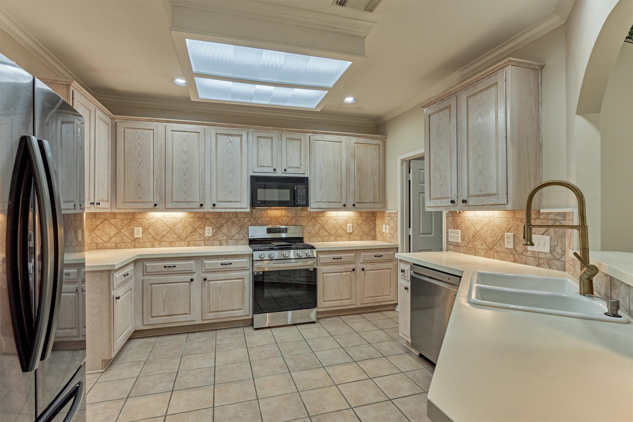 14420 Walters Road, Unit 26 Houston, TX 77014 - Photo 13 of 45 This kitchen features light wood cabinetry, new stainless steel refrigerator and stove, and ample counter space with a double sink. The tiled backsplash and flooring add a classic touch, complemented by under-cabinet lighting and a spacious layout.