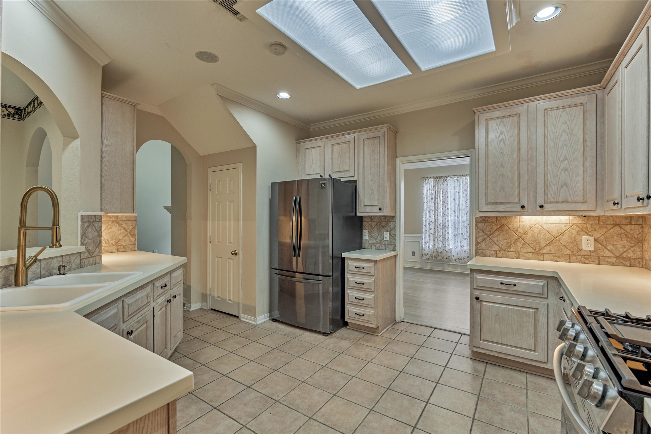14420 Walters Road, Unit 26 Houston, TX 77014 - Photo 17 of 45 This kitchen features light wood cabinetry, a stainless steel refrigerator, and a gas stove. It has a spacious layout with ample counter space and a dual sink, complemented by tiled flooring and backsplash. Natural light flows in through from the formal dining room.
