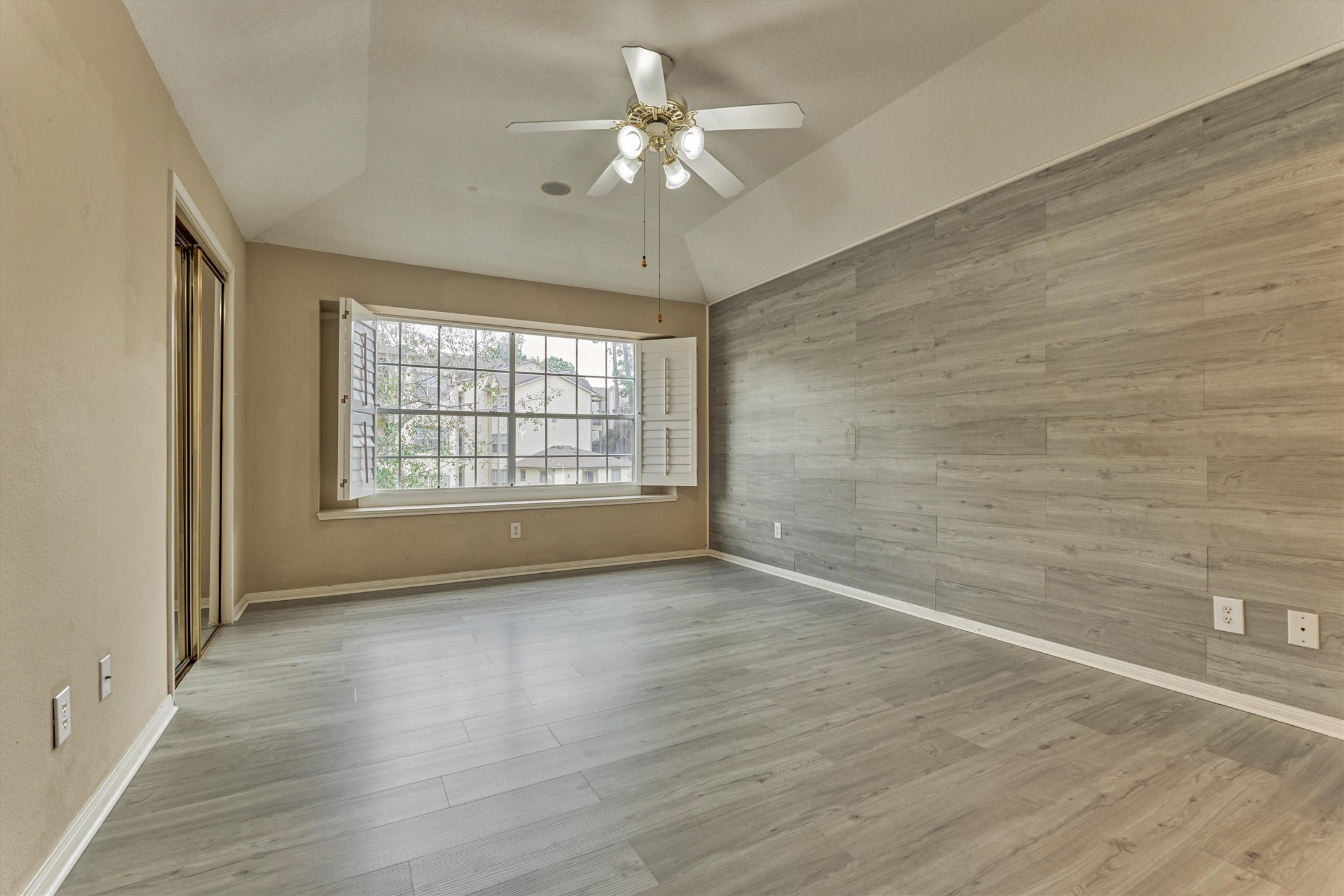 14420 Walters Road, Unit 26 Houston, TX 77014 - Photo 28 of 45 This bright primary bedroom features a large window with shutters, sleek gray wood-look flooring, and a modern ceiling fan. The accent wall adds a touch of style, making it a cozy and inviting space.