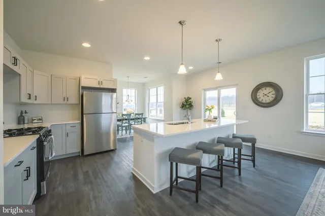 a kitchen with stainless steel appliances a refrigerator a stove a sink a dining table and chairs with wooden floor