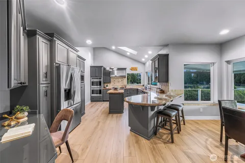 a dining hall with stainless steel appliances granite countertop a refrigerator a kitchen island furniture a dining table and chairs