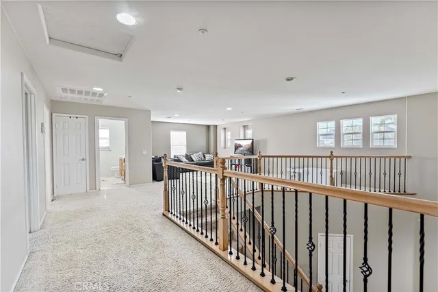 a view of a hallway with a livingroom with windows & a ceiling fan