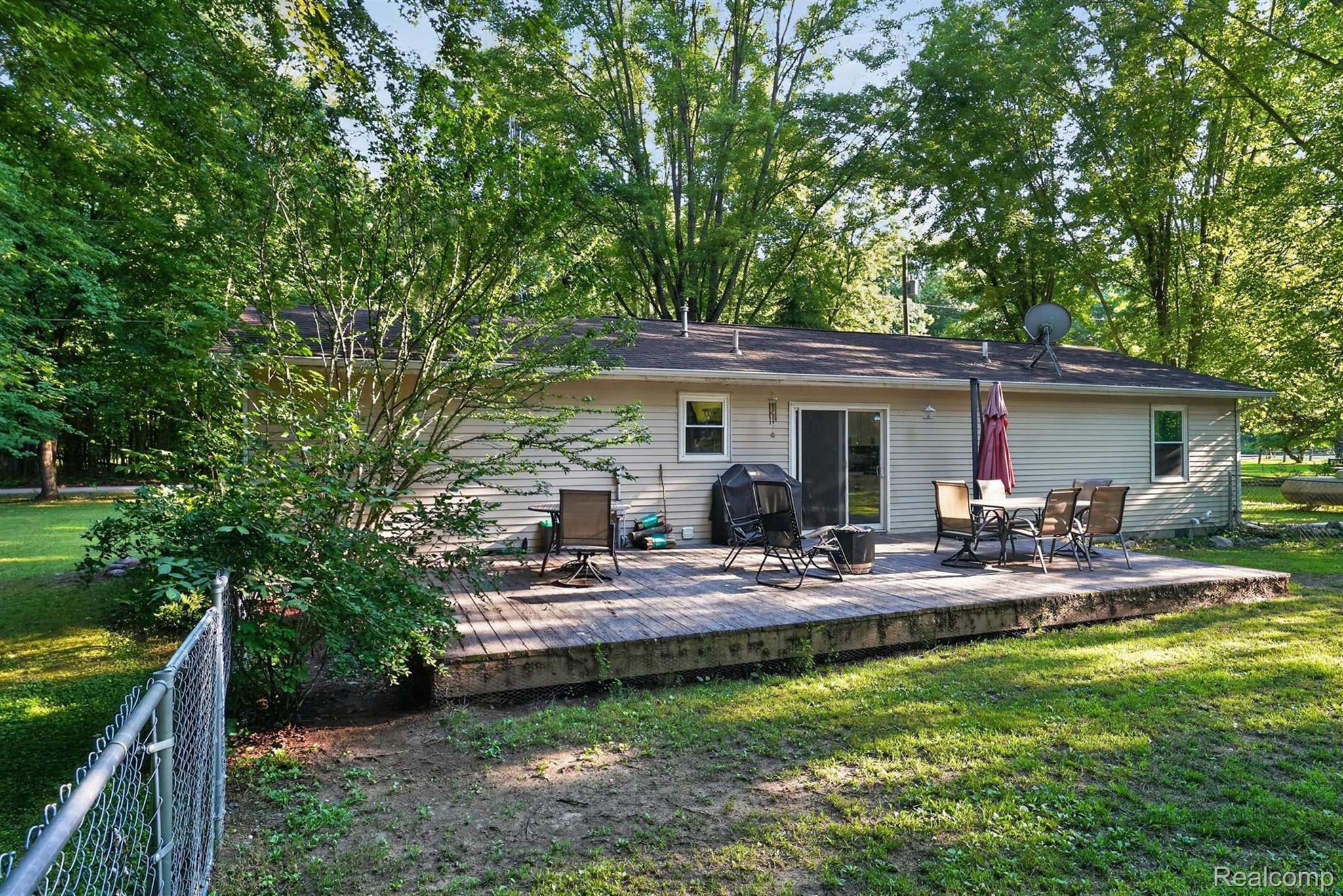 8696 West Sargent Road Fowlerville, MI 48836 - Photo 29 of 36 Expansive wood deck with a sliding glass door entry, surrounded by mature trees