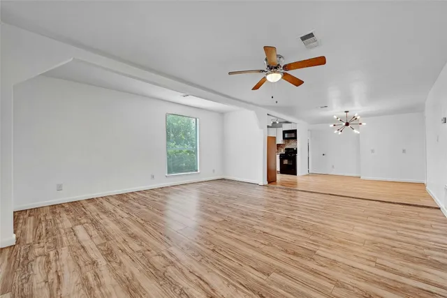 an empty room with wooden floor ceiling fan and windows