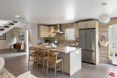 a kitchen with stainless steel appliances granite countertop a refrigerator a sink a stove a dining table and chairs with wooden floor