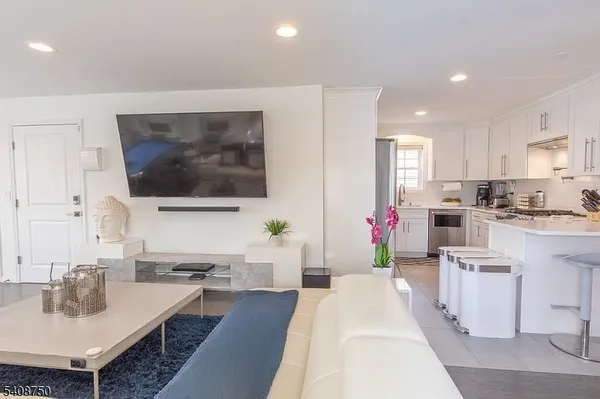 a living room with stainless steel appliances furniture a flat screen tv and a kitchen view