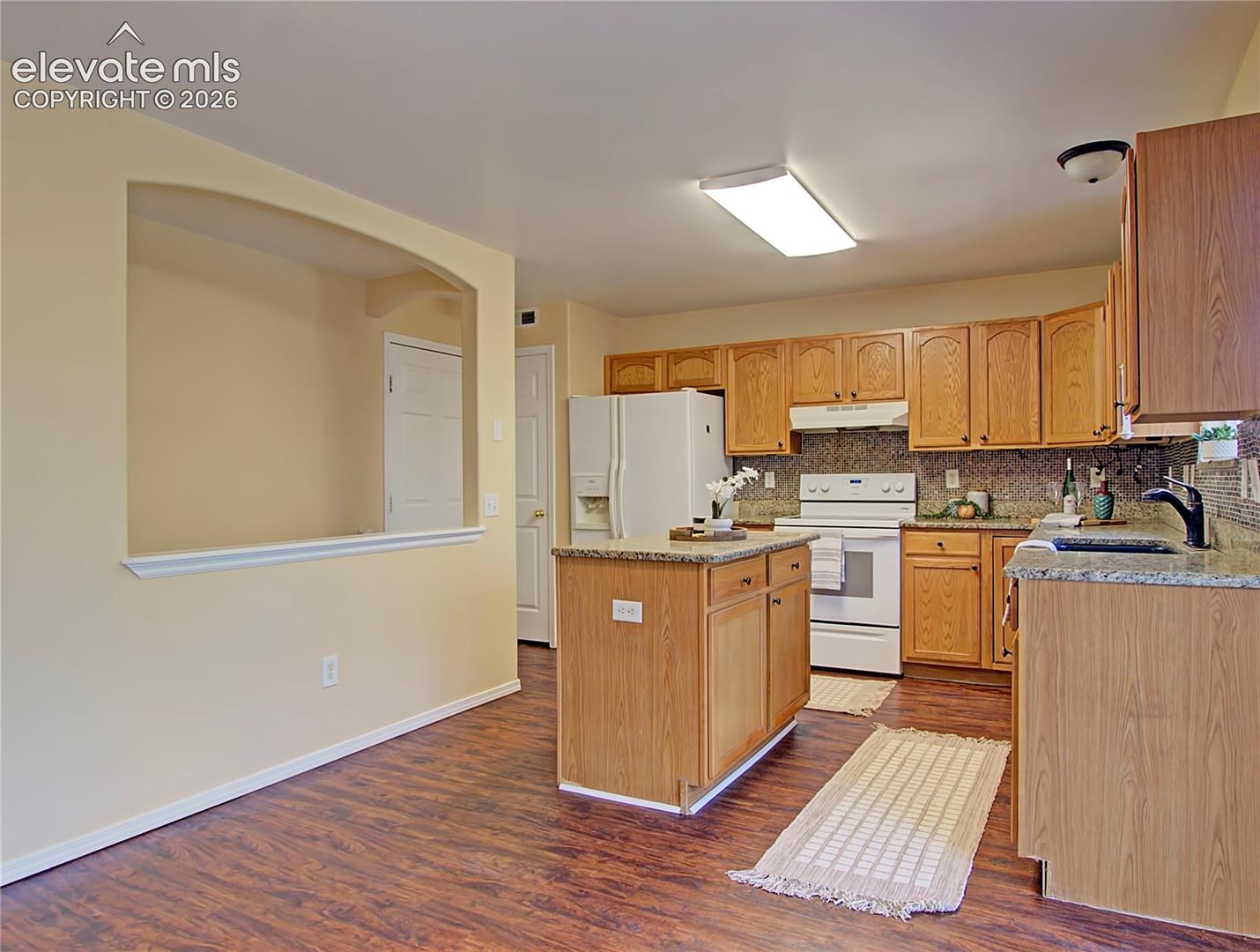 4886 Rusty Nail Point, Unit 101 Colorado Springs, CO 80916 - Photo 10 of 28 Kitchen featuring wood-finish flooring, light wood cabinetry, white appliances, and granite countertops