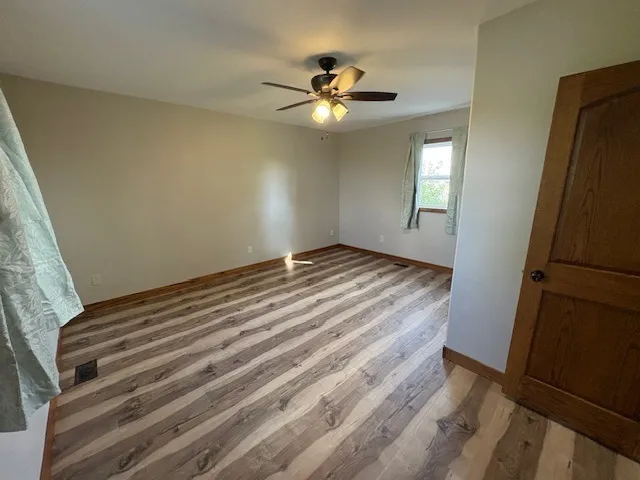 a view of an empty room with wooden floor and a ceiling fan