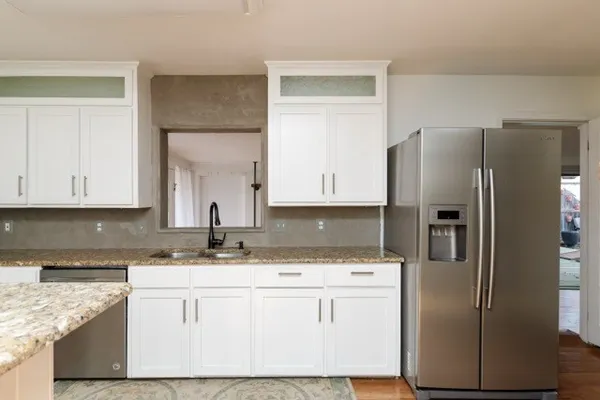 a kitchen with stainless steel appliances granite countertop a refrigerator a sink and white cabinets