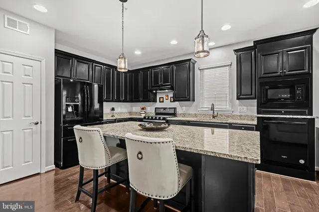 a kitchen with stainless steel appliances granite countertop a stove top oven a refrigerator a sink and chairs