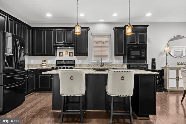 a kitchen with stainless steel appliances granite countertop a stove a sink a microwave a refrigerator and chairs