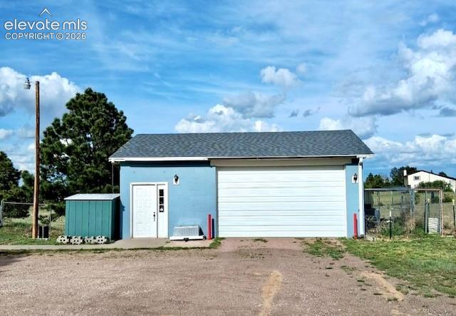 13335 Gymkhana Road Peyton, CO 80831 - Photo 37 of 38 Standalone garage structure featuring a light blue exterior, a large white garage door, and a white entry door with vertical window panels