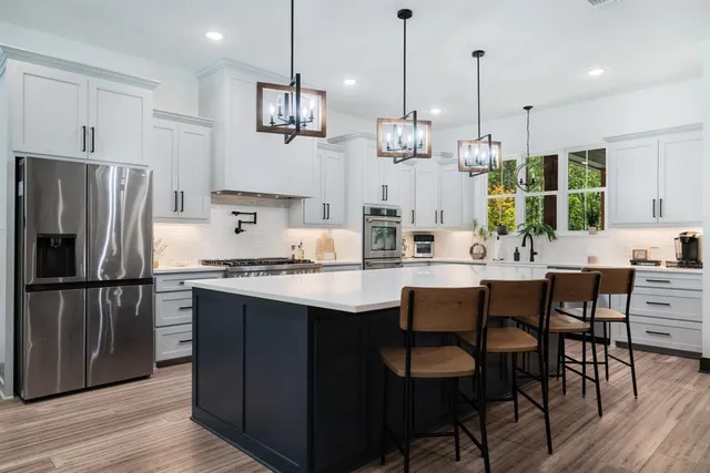 a kitchen with stainless steel appliances granite countertop a sink a stove a refrigerator and island wooden floor