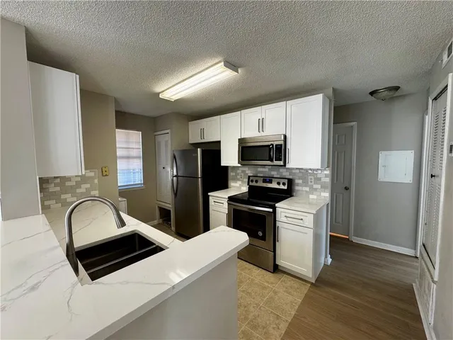 a kitchen with stainless steel appliances a sink a stove a microwave a refrigerator a cabinets and wooden floor