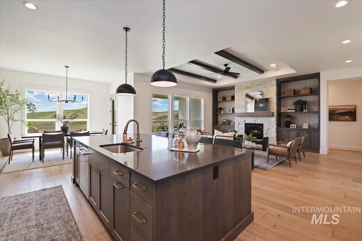 7615 Brown Way Eagle, ID 83714 - Photo 11 of 43 Open-concept living area with wood-finish flooring, a central kitchen island featuring a sink and pendant lighting, and a stone-clad fireplace flanked by built-in shelving
