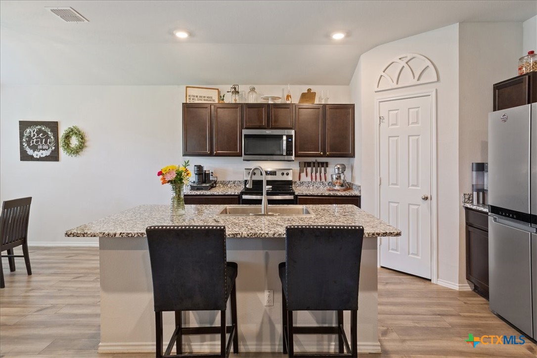 1000 Velvet Court Troy, TX 76579 - Photo 9 of 25 a kitchen with stainless steel appliances granite countertop a stove a refrigerator a sink a dining table and chairs with wooden floor