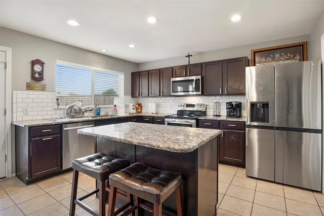 a kitchen with kitchen island granite countertop stainless steel appliances a sink a stove a refrigerator cabinets and a counter top space