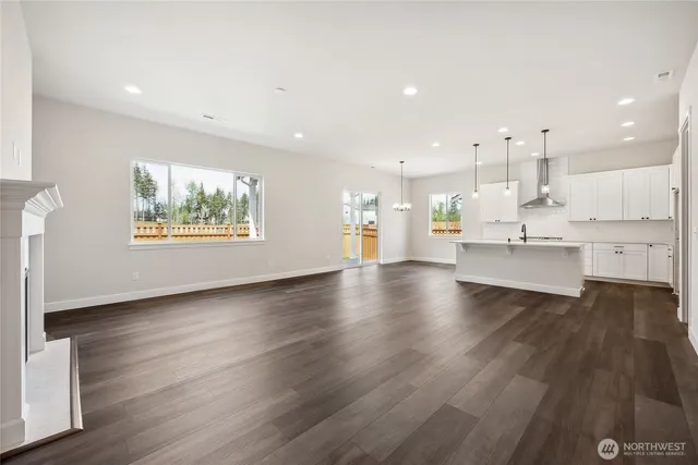 a view of an empty room and kitchen with wooden floor and windows