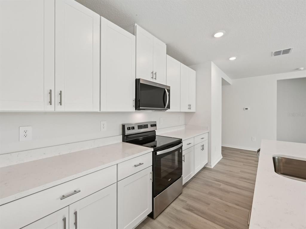 7628 Satterfield Terrace Parrish, FL 34219 - Photo 11 of 25 a kitchen with white cabinets stainless steel appliances and wooden floor