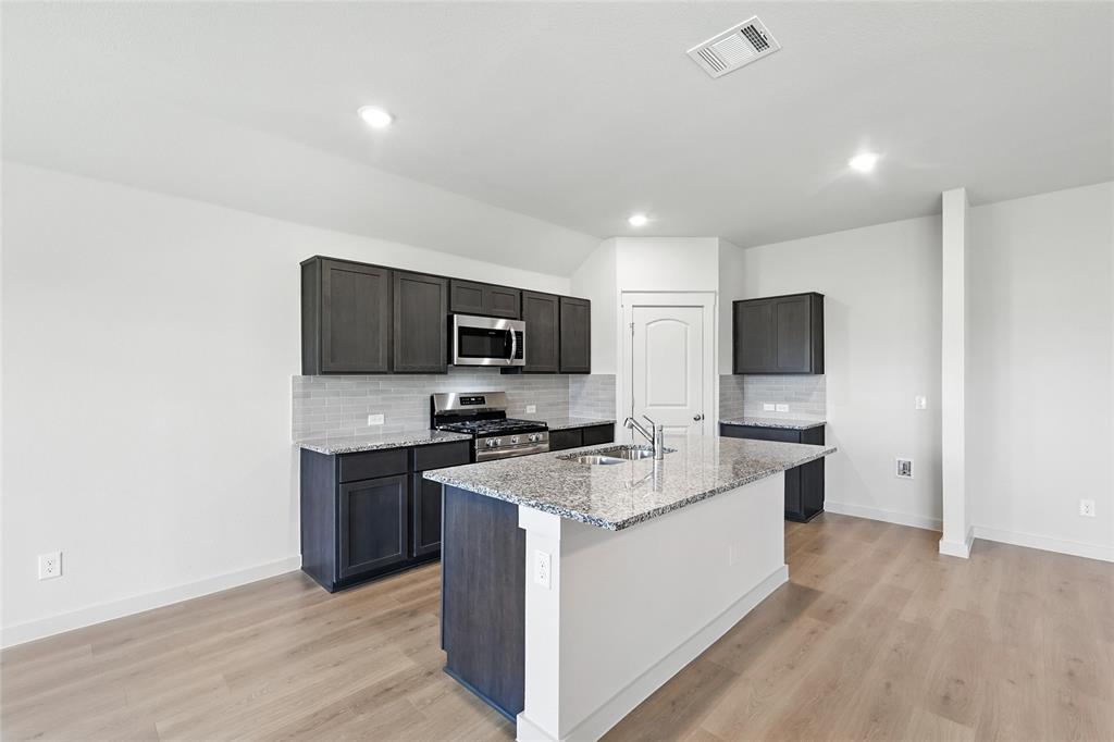 1795 Gleasondale Place Forney, TX 75126 - Photo 4 of 29 Kitchen featuring stainless steel appliances, light stone countertops, light wood finished floors, backsplash, and a kitchen island with sink